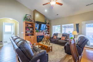 Living room featuring wood finished floors, arched walkways, high vaulted ceiling, ceiling fan, and a glass covered fireplace