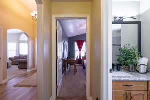 Hall featuring arched walkways, vaulted ceiling, carpet, wood finished floors, and a chandelier