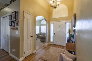 Entryway featuring wood finished floors, arched walkways, a towering ceiling, and a chandelier