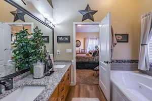 Bathroom with dark wood-style flooring, double vanity, a tub with jets, and ensuite bath