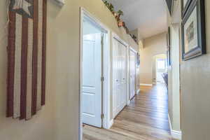Hallway with arched walkways, a textured wall, and light wood-style flooring