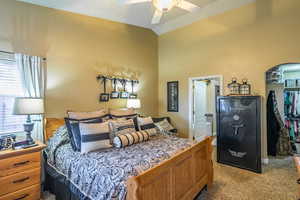 Carpeted bedroom featuring a walk in closet, vaulted ceiling, and ceiling fan
