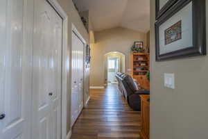 Corridor with arched walkways, lofted ceiling, and dark wood finished floors