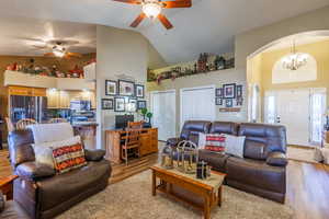 Living room with high vaulted ceiling, light wood-style floors, a ceiling fan, arched walkways, and a chandelier
