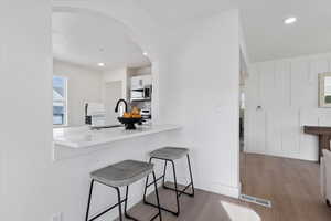 Kitchen with arched walkways, wood finished floors, a breakfast bar area, white cabinets, and stainless steel microwave