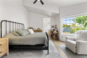 Bedroom with vaulted ceiling, light wood finished floors, and a ceiling fan