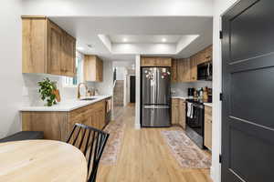 Kitchen with stainless steel appliances, light wood-style floors, a tray ceiling, recessed lighting, and brown cabinetry