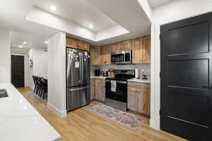 Kitchen featuring stainless steel appliances, light wood-style flooring, recessed lighting, brown cabinets, and a tray ceiling
