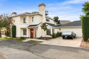 Traditional home featuring a chimney, stucco siding, concrete driveway, and a shingled roof