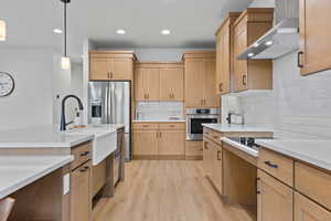 Kitchen featuring hanging light fixtures, tasteful backsplash, light wood finished floors, wall chimney range hood, and recessed lighting
