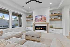 Living room featuring a glass covered fireplace, ceiling fan, recessed lighting, and light colored carpet