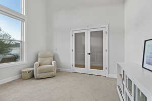 Office with healthy amount of natural light, light colored carpet, french doors, and a towering ceiling