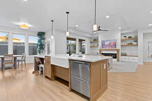 Kitchen featuring light stone counters, a glass covered fireplace, decorative light fixtures, light wood-style floors, and recessed lighting