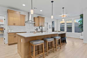 Kitchen featuring backsplash, decorative light fixtures, light wood-style flooring, recessed lighting, and a breakfast bar