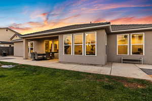 Back of property at dusk with a patio, stucco siding, and a lawn