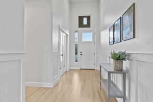 Foyer entrance featuring light wood finished floors, a high ceiling, wainscoting, and a decorative wall