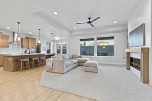 Living area with a glass covered fireplace, recessed lighting, a ceiling fan, light wood finished floors, and a tray ceiling
