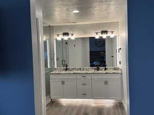 Ensuite bathroom with a textured ceiling, light wood-style flooring, double vanity, and a shower stall