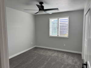 Spare room with dark carpet, a ceiling fan, and a textured ceiling