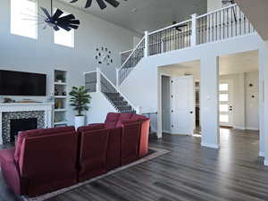 Living area with a high ceiling, LVP floors, a tile fireplace, stairway, and ceiling fan
