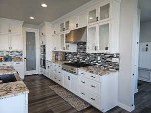 Kitchen with white cabinets, under cabinet range hood, light granite counters, appliances with stainless steel finishes, and dark wood-style flooring
