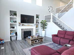 Living room with a fireplace, LVP floors, a towering ceiling, built in features, and stairs
