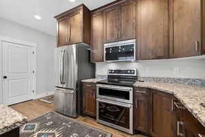 Kitchen featuring stainless steel appliances, light stone countertops, light wood-style floors, dark wood cabinetry, and recessed lighting