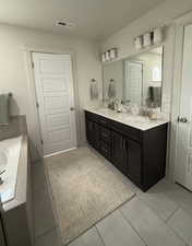 Bathroom with double vanity, light tile patterned flooring, a textured ceiling, and tiled tub