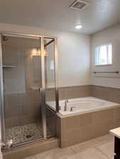 Full bathroom featuring light tile patterned flooring, a stall shower, a textured ceiling, a garden tub, and vanity