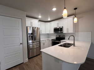 Kitchen featuring a peninsula, stainless steel appliances, white cabinets, dark wood-style flooring, and a textured ceiling
