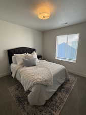 Bedroom with dark carpet and a textured ceiling