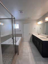 Bathroom with double vanity, a textured ceiling, a bath, light tile patterned floors, and a stall shower