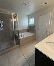 Full bathroom featuring double vanity, a stall shower, a bath, light tile patterned flooring, and a textured ceiling