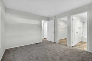 Unfurnished bedroom with light carpet, a walk in closet, and ensuite bath