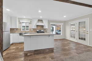 Kitchen with white cabinets, tasteful backsplash, stainless steel appliances, a kitchen island, and ornamental molding