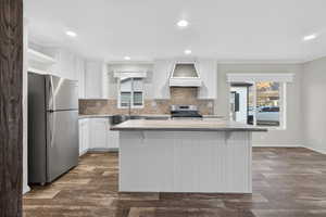 Kitchen with white cabinetry, decorative backsplash, appliances with stainless steel finishes, a kitchen island, and open shelves