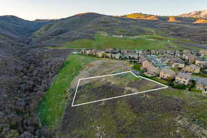 Aerial view of property and surrounding area featuring property boundaries highlighted, nearby suburban area, and a mountain backdrop