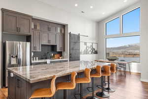 Kitchen featuring a barn door, light stone counters, backsplash, stainless steel fridge with ice dispenser, and dark brown cabinets
