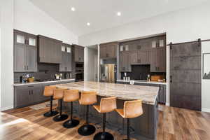 Kitchen with tasteful backsplash, glass insert cabinets, light stone countertops, a barn door, and stainless steel appliances
