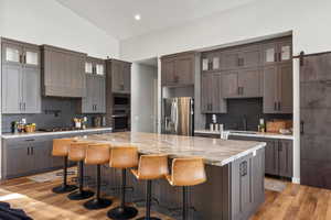 Kitchen with glass insert cabinets, backsplash, light stone counters, stainless steel appliances, and a kitchen bar