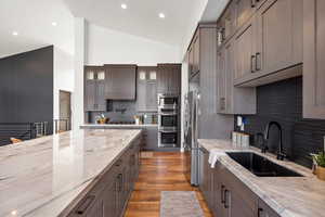 Kitchen with tasteful backsplash, light stone countertops, glass insert cabinets, stainless steel appliances, and recessed lighting