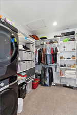 Spacious closet featuring attic access, stacked washer / drying machine, and light colored carpet