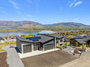 View of front of property featuring a garage, roof mounted solar panels, driveway, stone siding, and a water and mountain view
