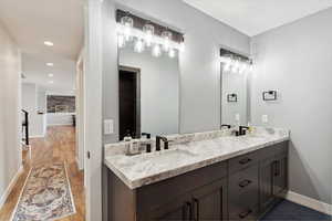 Bathroom with double vanity, recessed lighting, and dark wood-style flooring