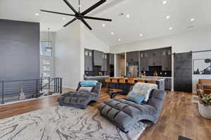 Living area with a barn door, high vaulted ceiling, recessed lighting, dark wood finished floors, and a ceiling fan