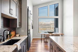 Kitchen with light stone counters, a barn door, dark wood-style flooring, a water view, and dark brown cabinetry