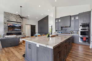 Kitchen with a breakfast bar, a barn door, glass insert cabinets, high vaulted ceiling, and a fireplace
