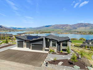 View of front of home with stone siding, a garage, driveway, roof mounted solar panels, and a water and mountain view