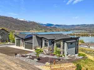 View of front of home featuring stone siding, a garage, driveway, a shingled roof, and a water and mountain view