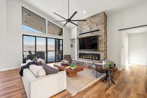 Living area featuring a towering ceiling, a fireplace, ceiling fan, and wood-type flooring